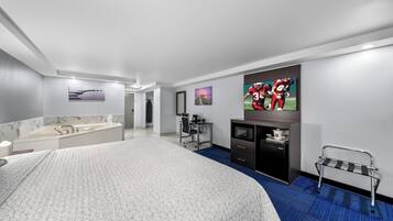 Habitación de hotel moderna con una cama grande, un baño con tocador de mármol, un escritorio con silla, un televisor en la pared y un banco junto a la ventana.