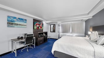 Une chambre d’hôtel avec un grand lit, un bureau avec une chaise, une télévision, une armoire et une fenêtre avec des rideaux.