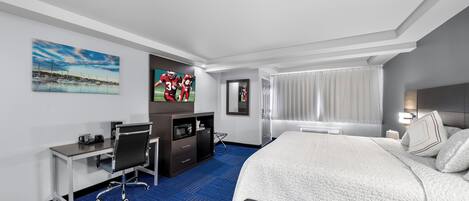 A hotel room with a large bed, a desk with a chair, a TV, a wardrobe, and a window with curtains.