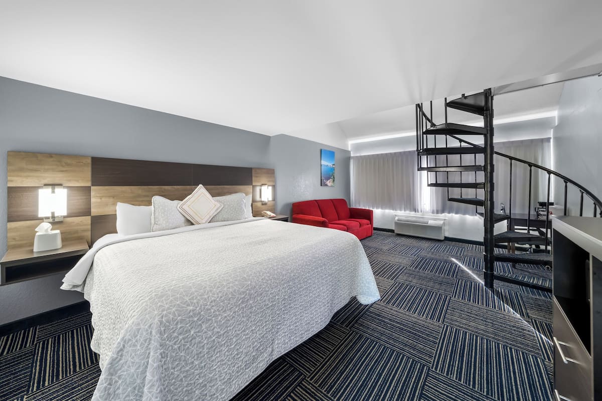 A hotel room with a large bed, a red chair, a spiral staircase, and a view of the city.