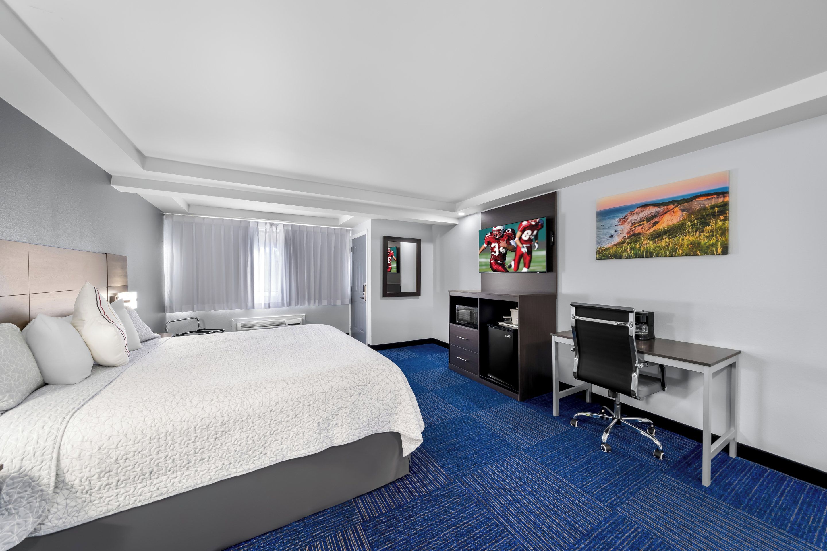 A hotel room with a large bed, a desk with a chair, a television, and artwork on the walls.
