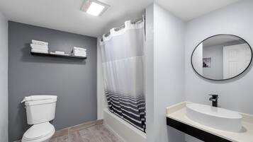 Un baño con inodoro, ducha con cortina a rayas, lavamanos con espejo y repisa con toallas.