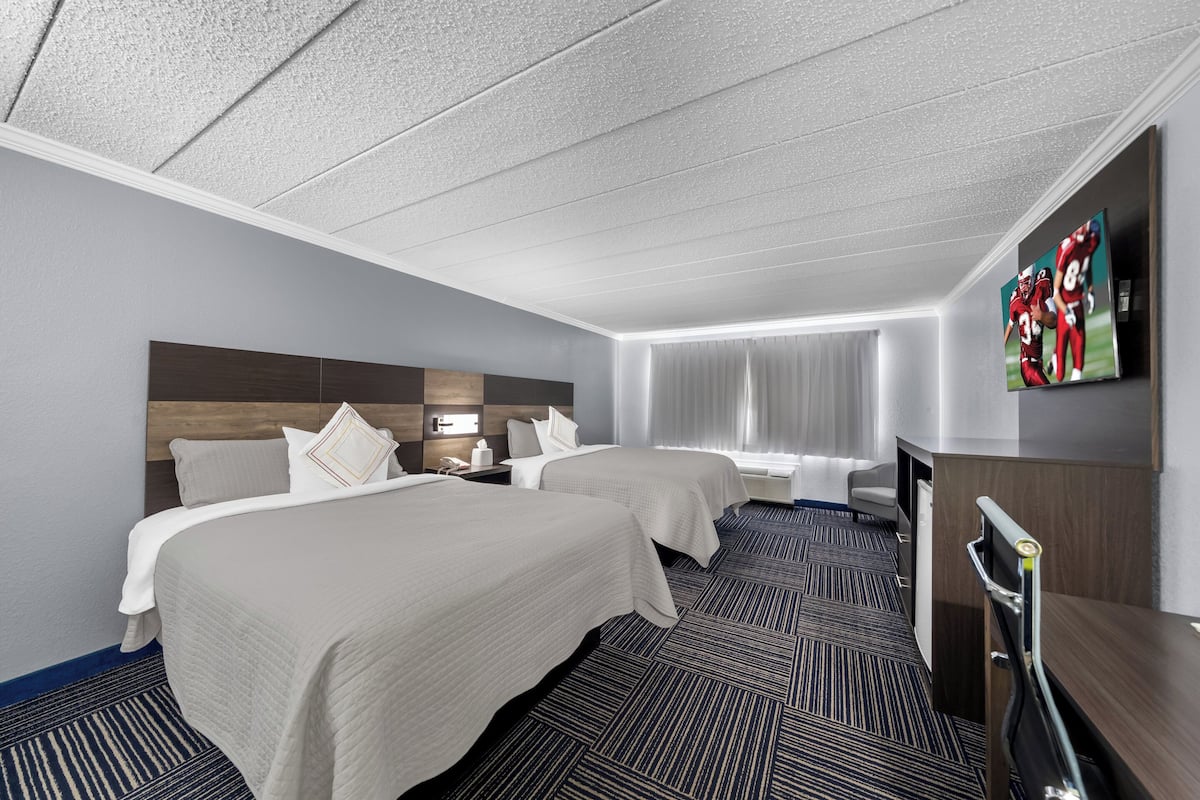 A hotel room with two beds, a desk, a TV, and a window with curtains.