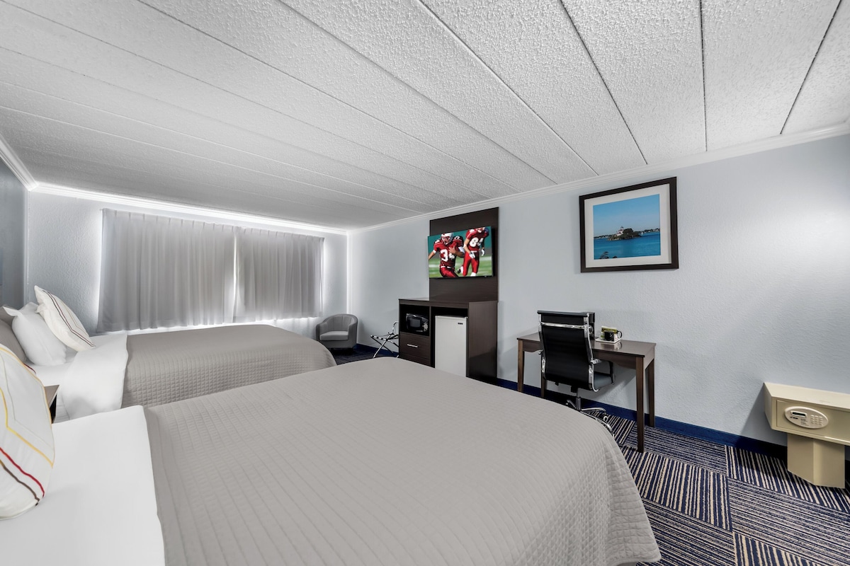 A hotel room with two beds, a desk, a chair, a TV, and a picture on the wall.