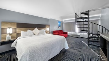Habitación de hotel con una cama grande, una silla roja, una escalera de caracol y vistas a la ciudad.