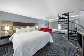 A hotel room with a large bed, a red chair, a spiral staircase, and a view of the city. - Admiralty Inn & Suites - a Red Collection Hotel (East Falmouth)