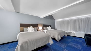 Ein Hotelzimmer mit zwei Betten, einem blauen Teppich, einem Holz-Kopfteil, einem Nachttisch mit Lampe und einem Fenster mit Vorhängen.