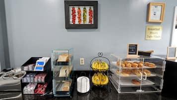 Een ontbijtbuffet met diverse gerechten, een bord met de ontbijttijden en een foto in een lijst aan de muur.