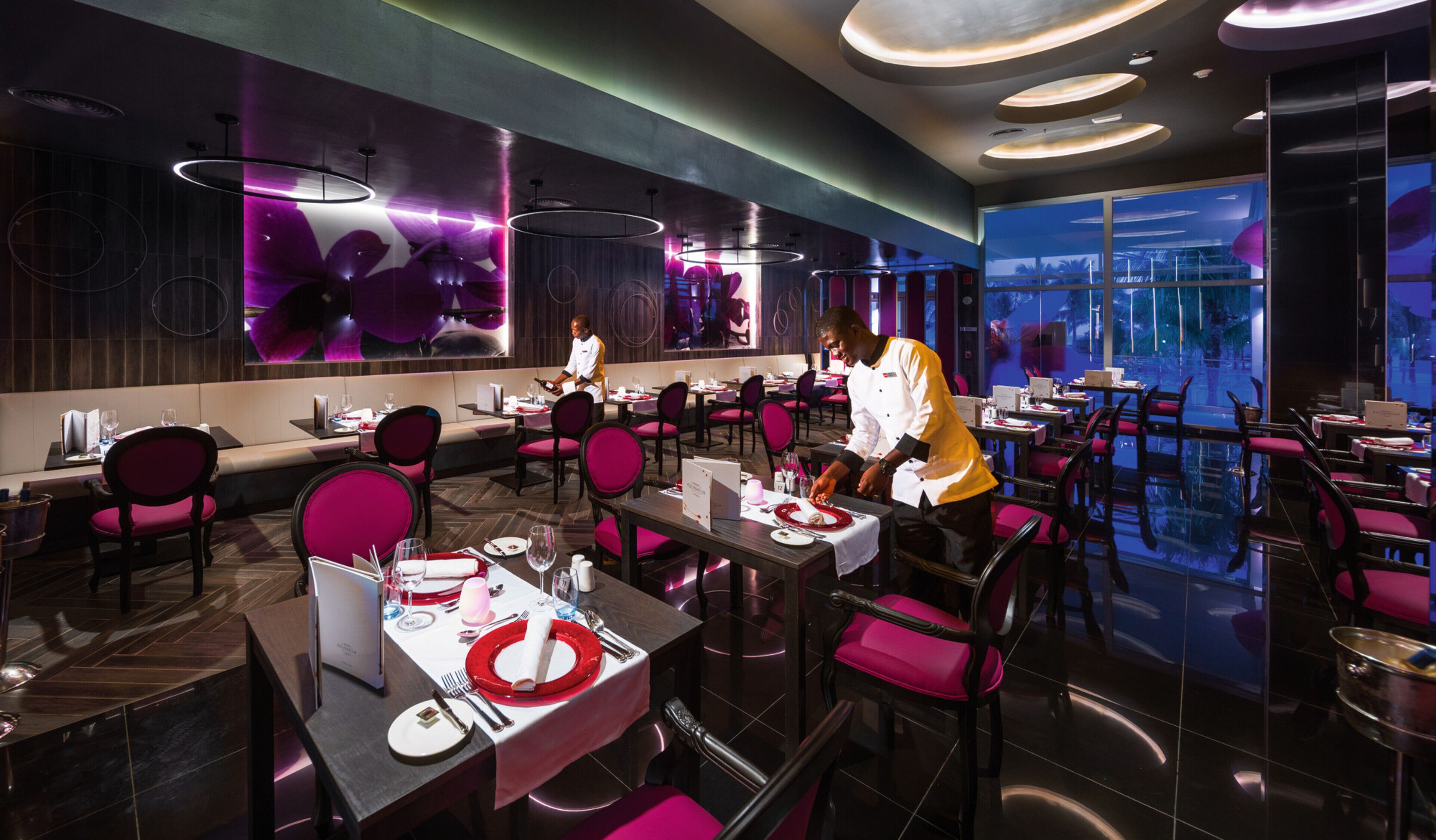 Ein modernes Restaurant mit hohen Tischen und Stühlen, einem großen Bildschirm und Blick auf die Stadtlandschaft.