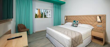 A hotel room with a bed, a desk, a chair, a TV, a ceiling fan, and a window with curtains.