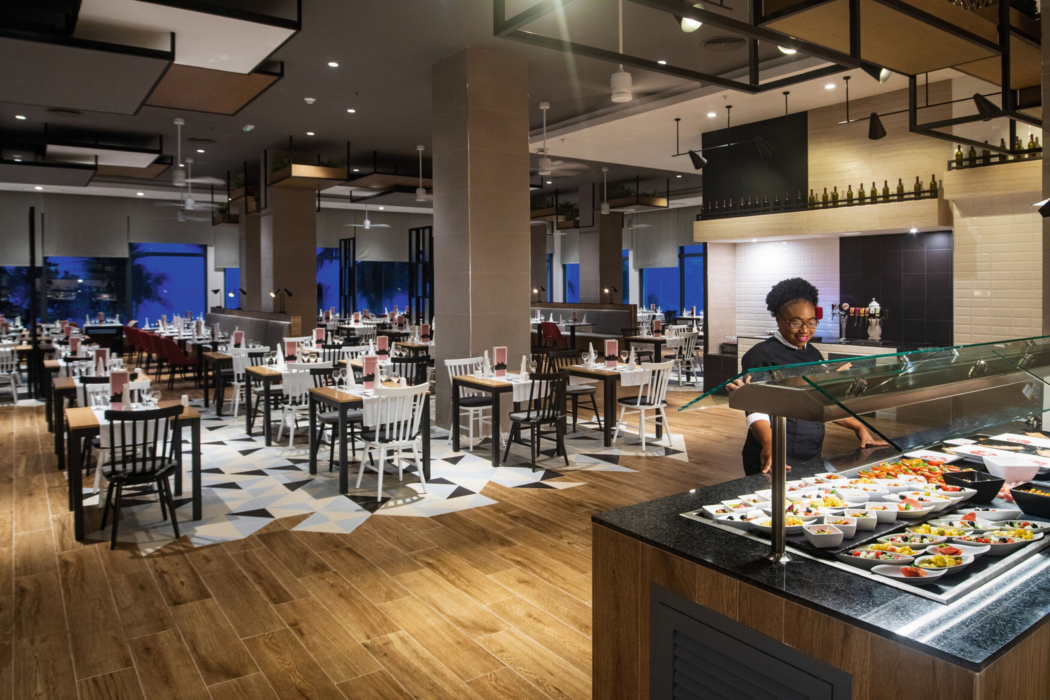 A modern restaurant with a buffet area, multiple dining tables, and a variety of food options.
