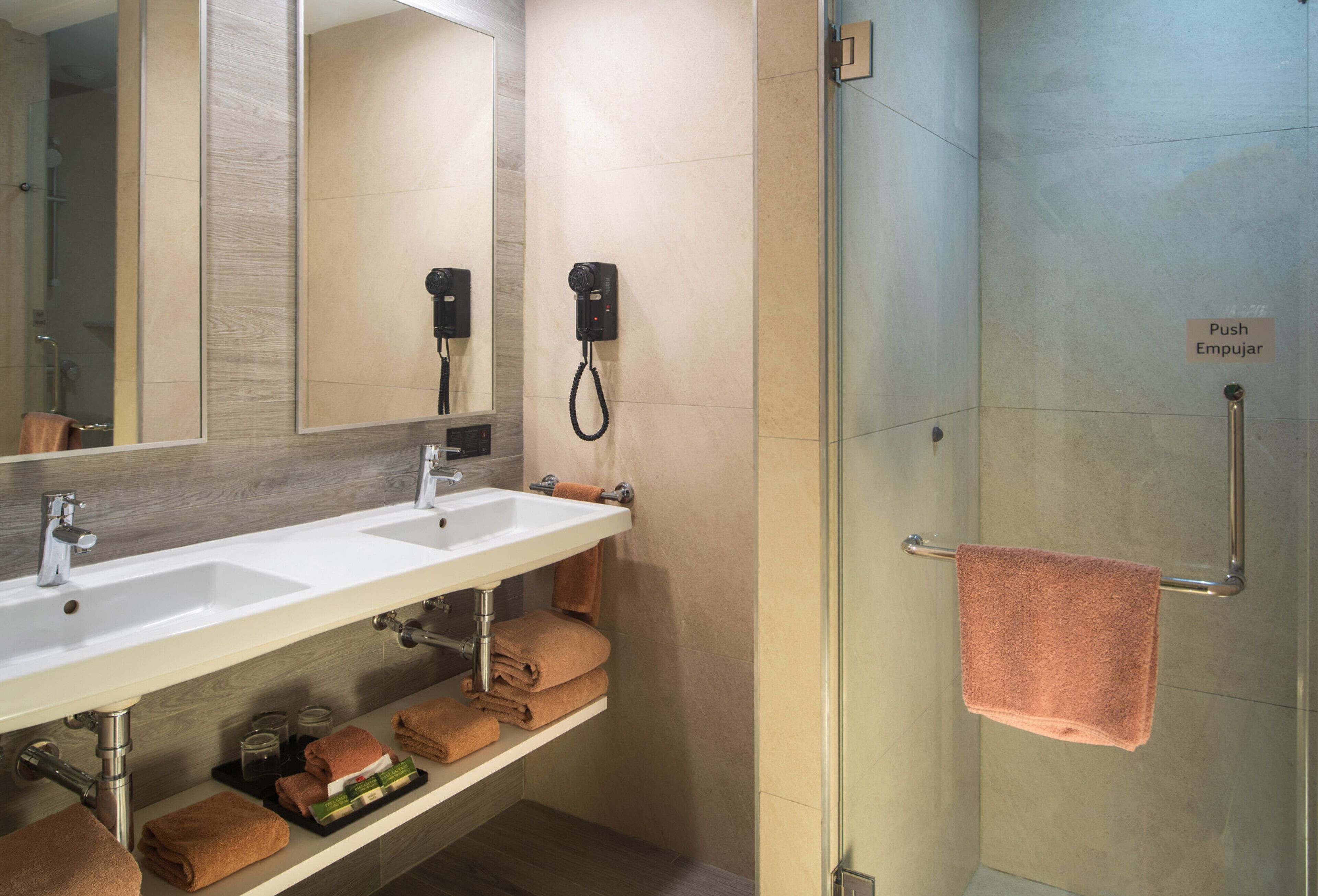 A bathroom with a double sink, towel rack, and a push button for the shower.