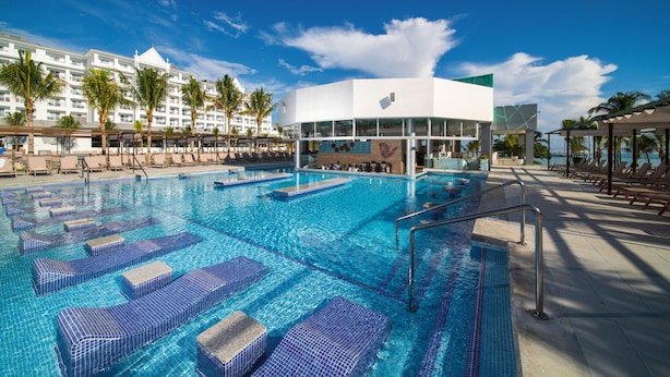 A swimming pool with lounge chairs, a modern building, and palm trees. - Hotel Riu Ocho Rios - All Inclusive (Ocho Rios)