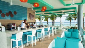 A bar area with a view of the ocean, bar stools, and a seating area with teal cushions. - Hotel Riu Ocho Rios - All Inclusive (Ocho Rios)