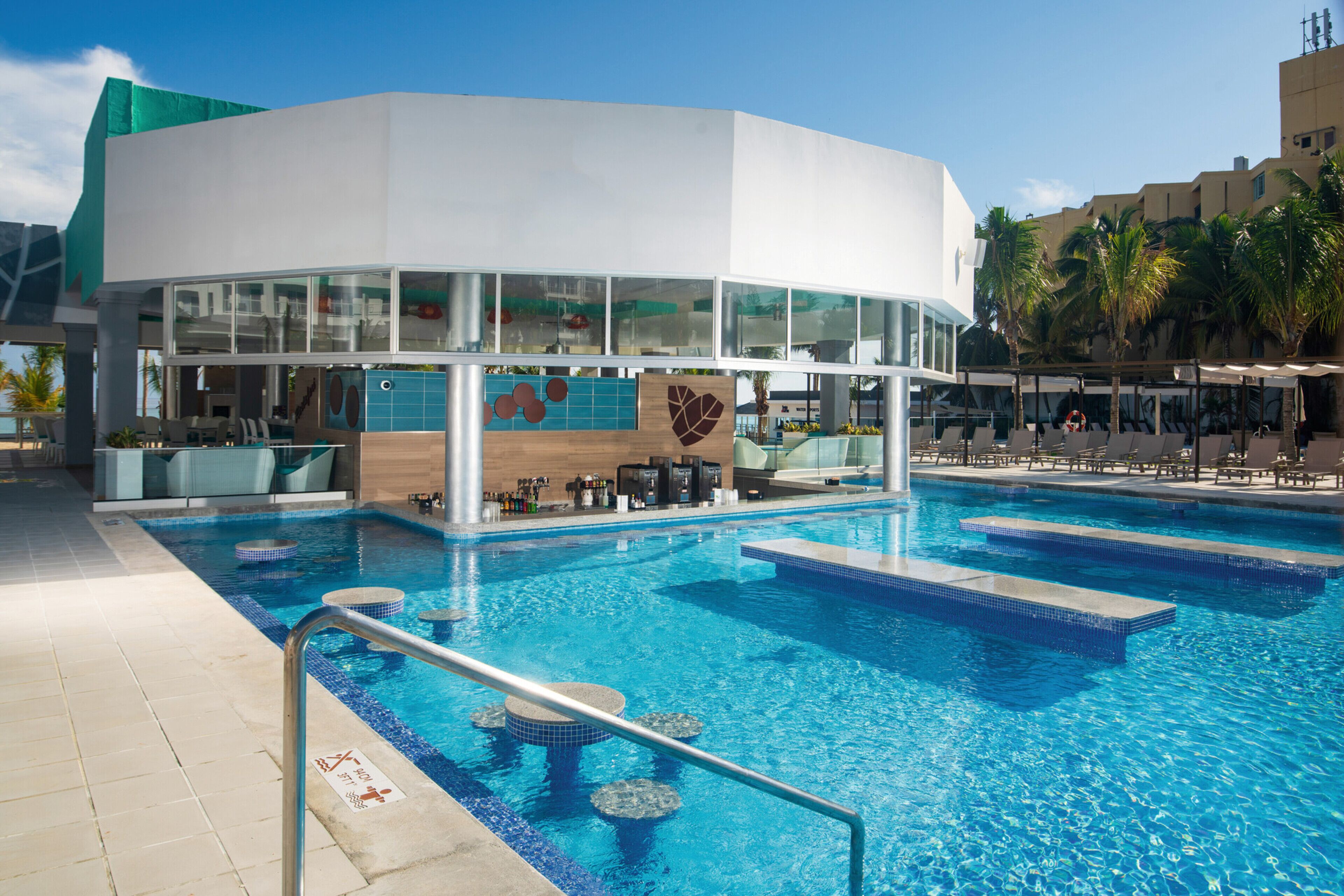 Un espace piscine moderne, comprenant un bar, des chaises longues et une piscine à l’eau cristalline.