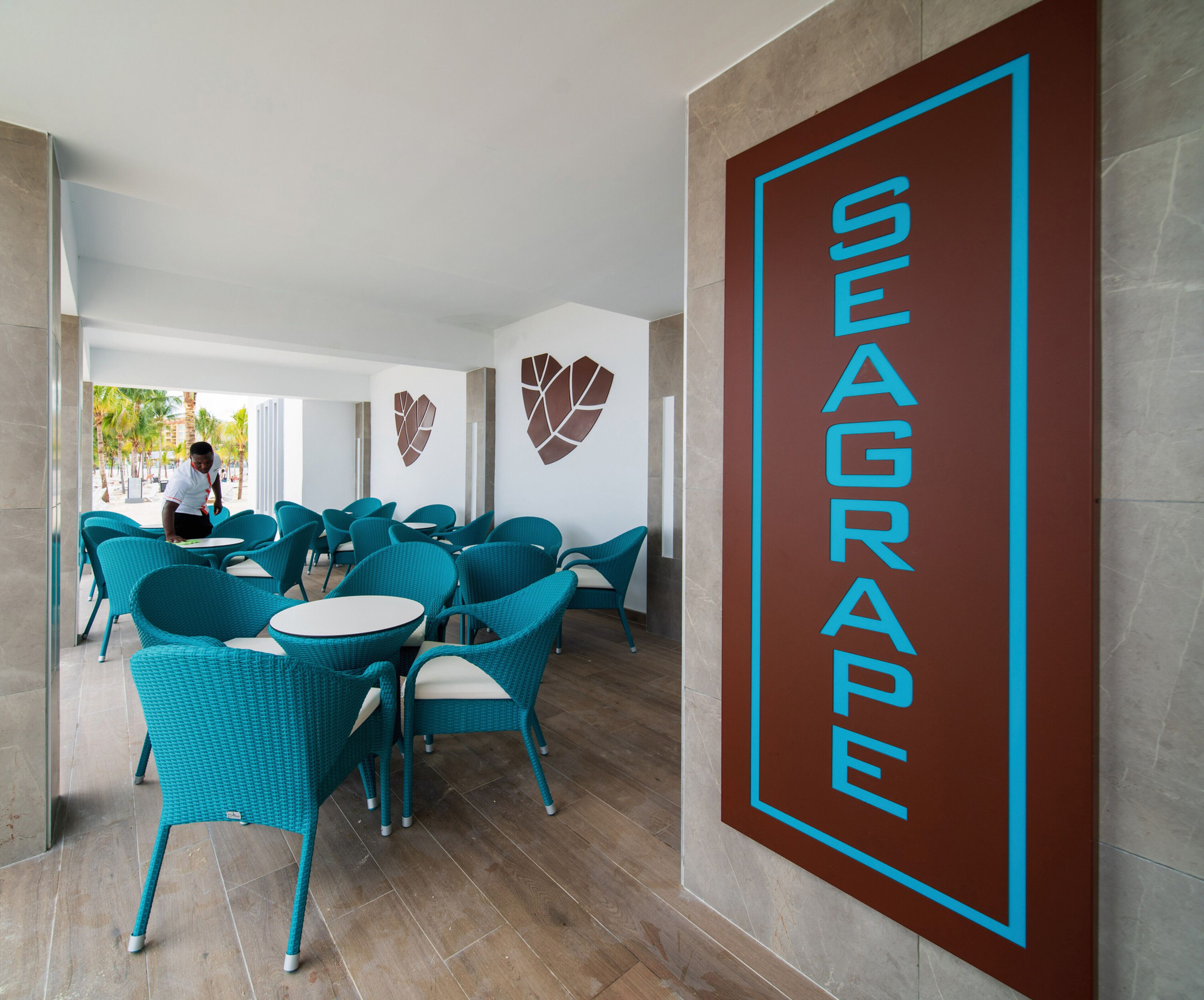 Vestíbulo de un hotel Seagrape con sillas color turquesa, mesas blancas y un cartel grande en la pared.
