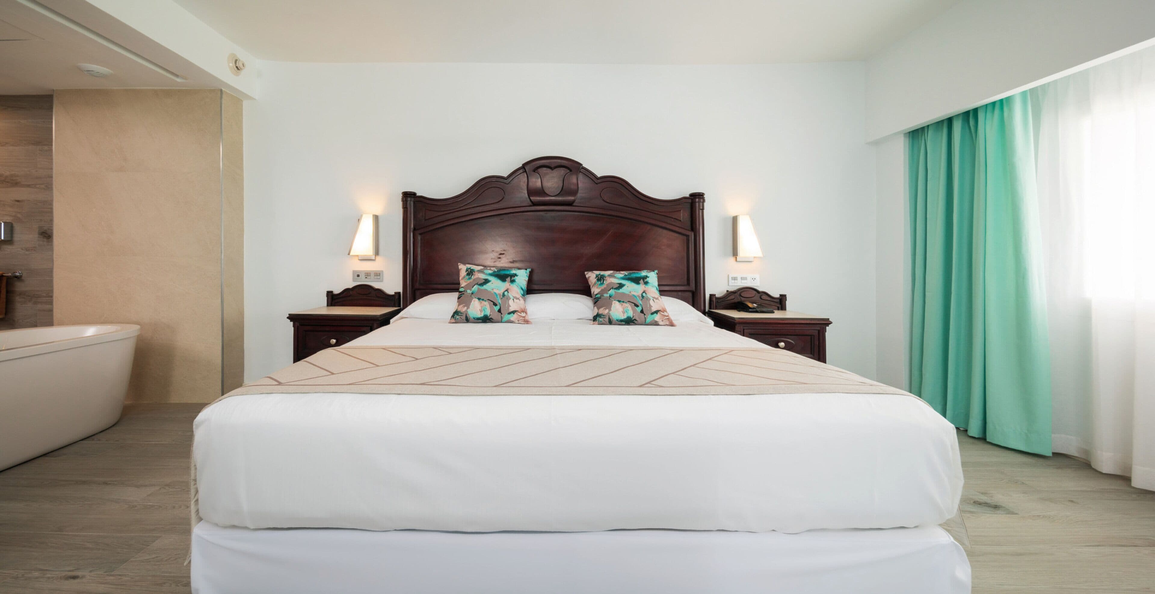 Habitación de hotel con una cama grande, una mesita de noche, una lámpara de pared y un baño con bañera.