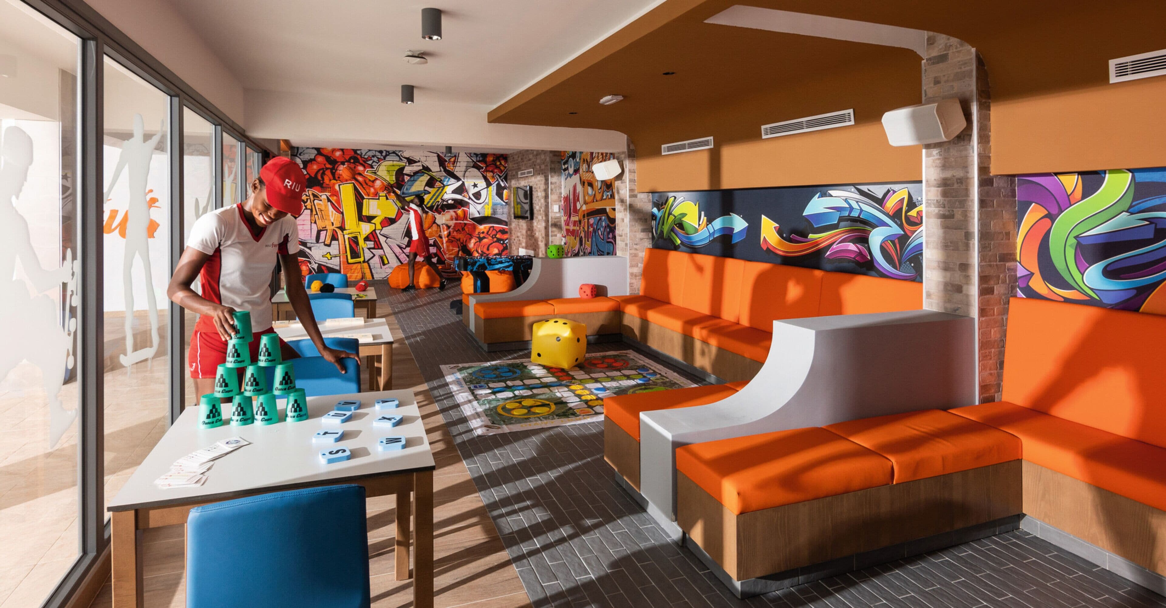 A vibrant indoor space with orange seating, a table with alphabet blocks, and colorful graffiti on the walls.