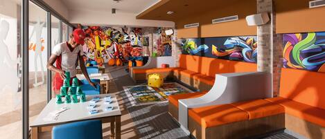 A vibrant indoor space with orange seating, a table with alphabet blocks, and colorful graffiti on the walls.