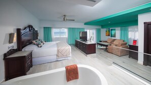 A modern hotel room with a large bed, a TV, a sofa, and a bathtub.