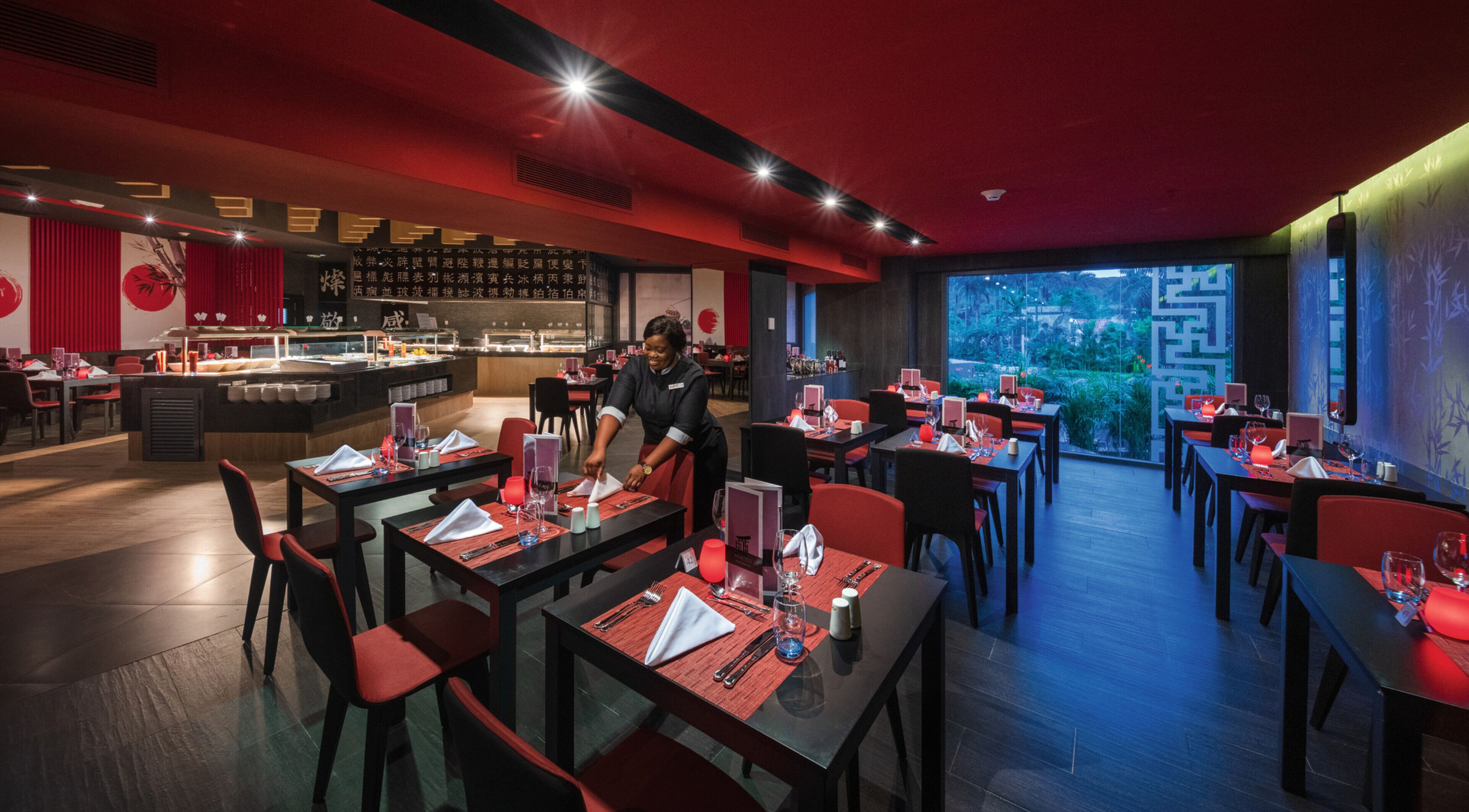 Ein Restaurant mit gedeckten Tischen, einer Bar und Blick auf Grünflächen.