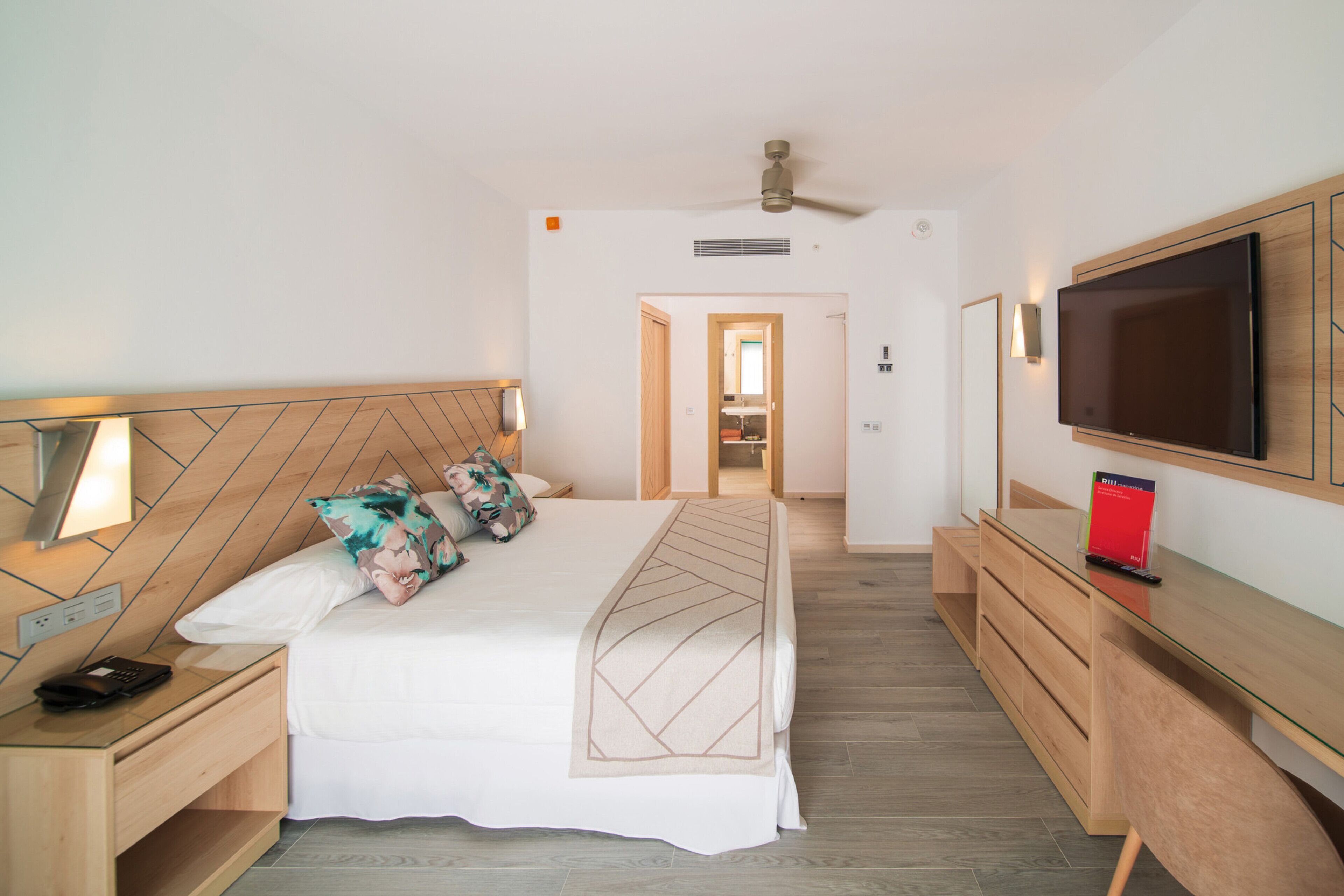 A hotel room with a bed, bedside tables, a TV, and a desk.