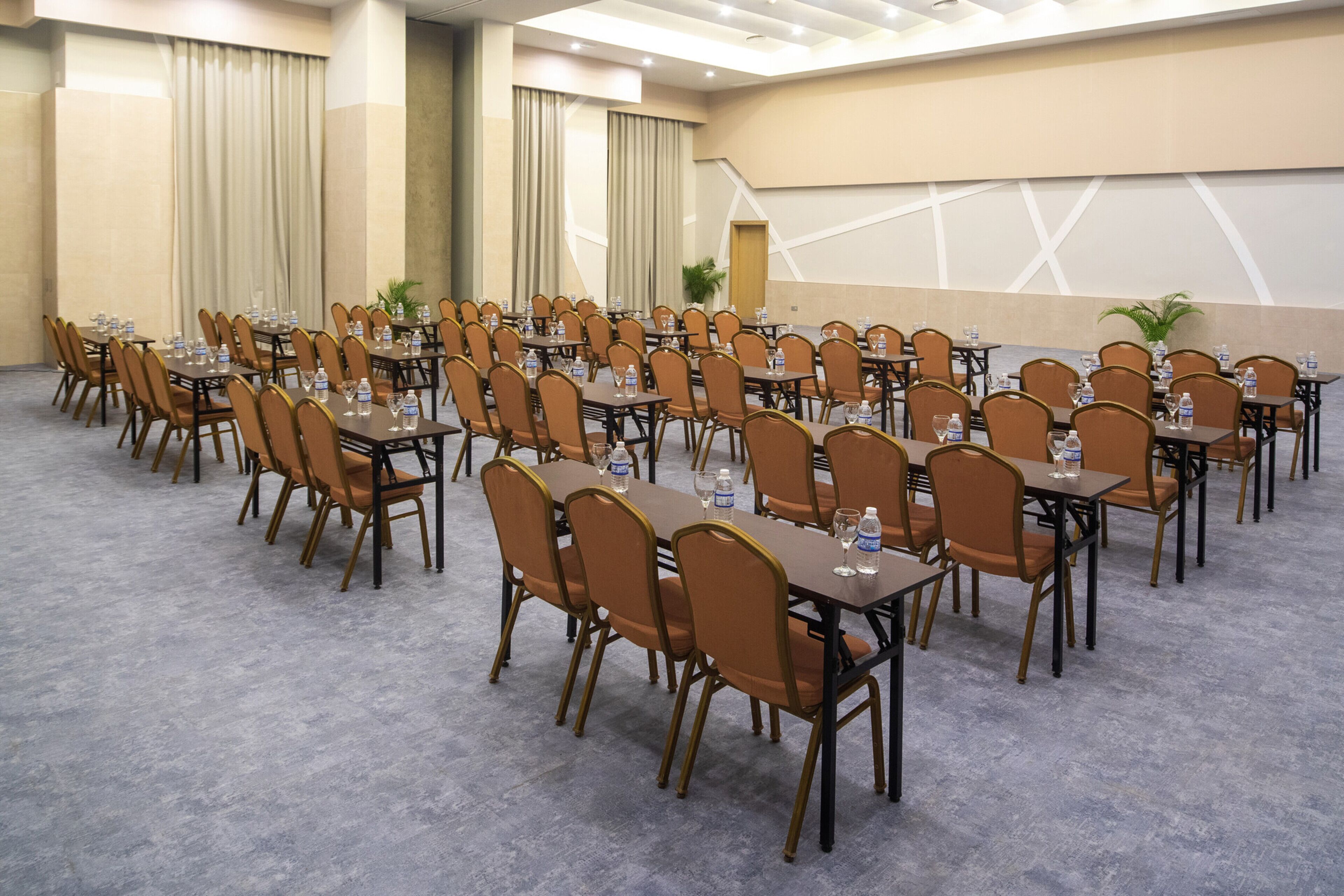 A conference room with rows of tables and chairs, water bottles, and a large screen at the front.