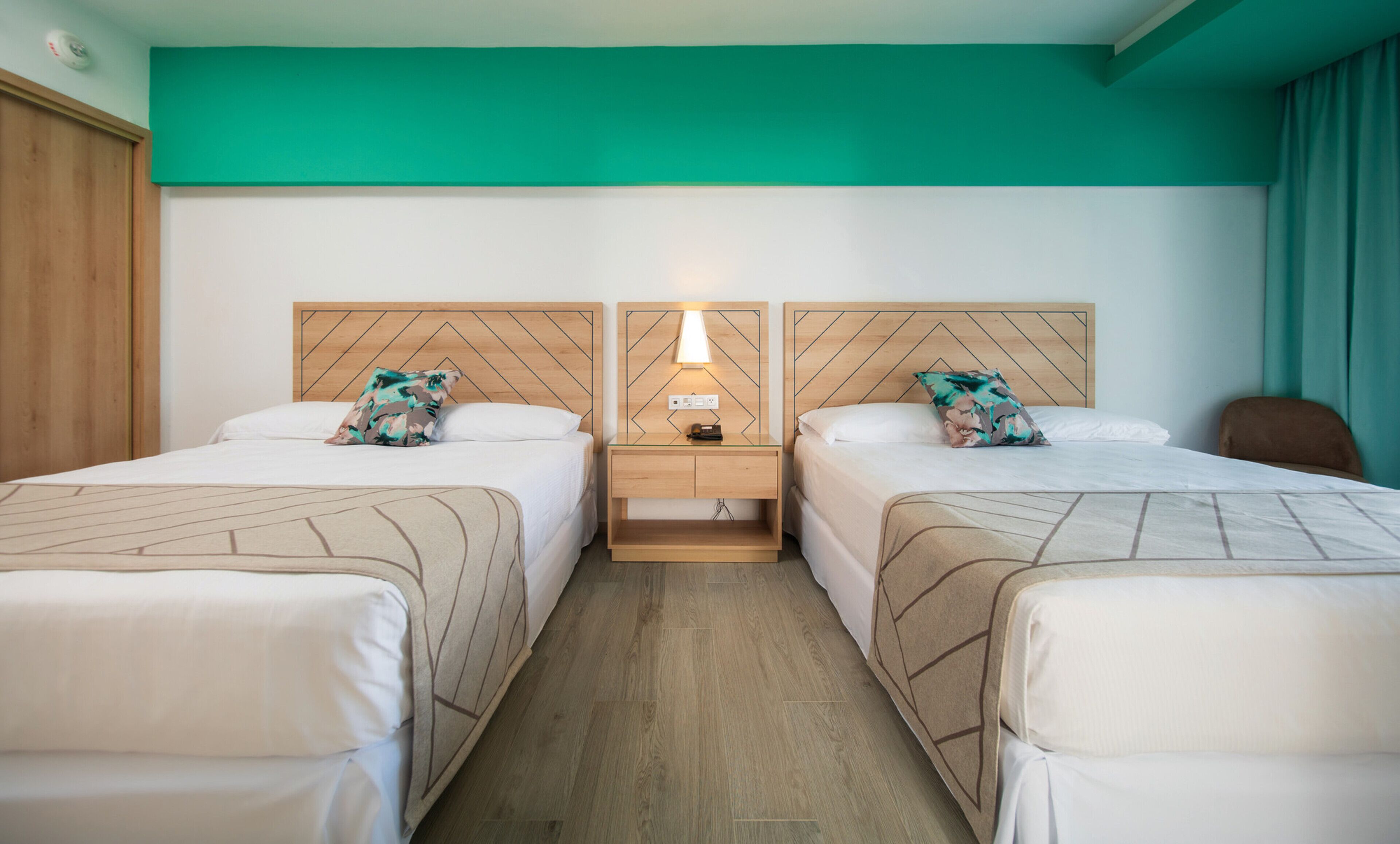 Quarto de hotel com duas camas, uma mesa de cabeceira com abajur e cabeceira de madeira.
