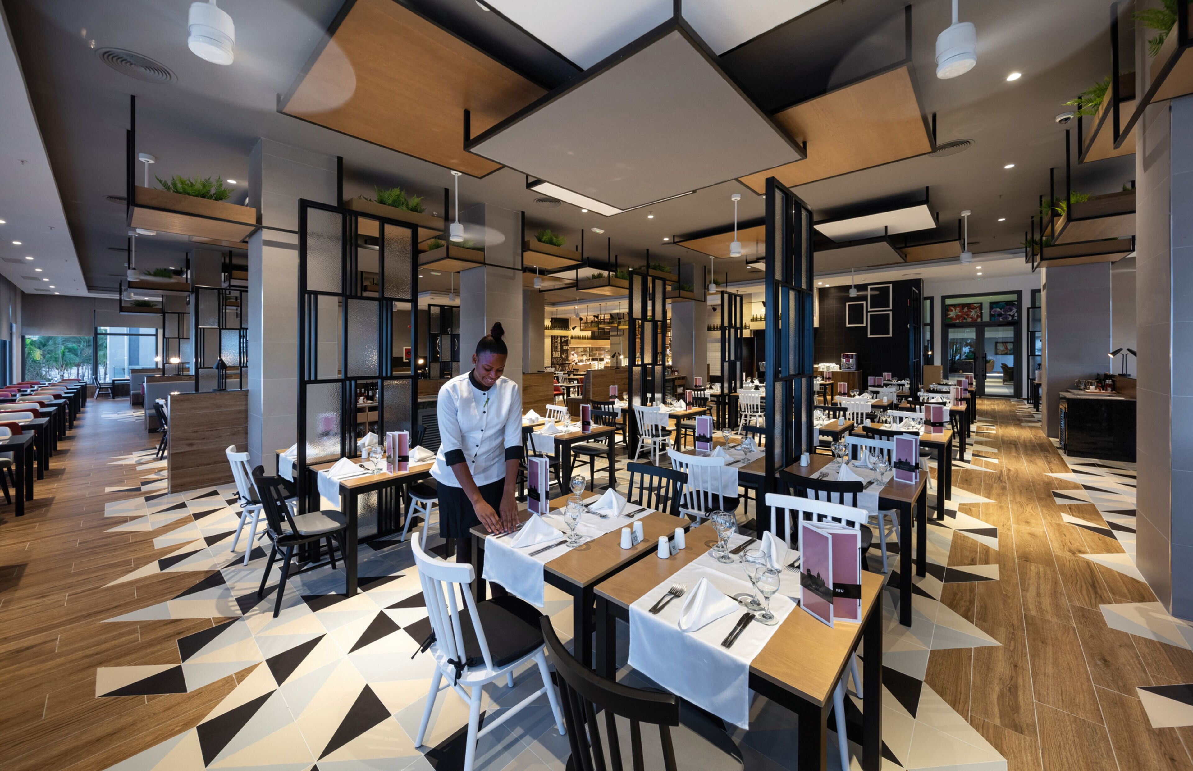 A modern restaurant with multiple dining tables, white chairs, and a geometric patterned floor.