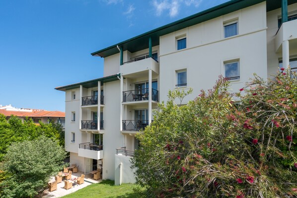 Un edificio de varios pisos con balcones, mobiliario exterior y vegetación.