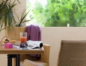 Una silla de mimbre, una mesa con un vaso de jugo de naranja, una revista y un par de gafas de sol.