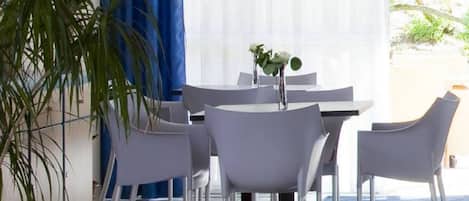 Un comedor con una mesa y sillas, una planta en maceta y un ventanal con cortinas.