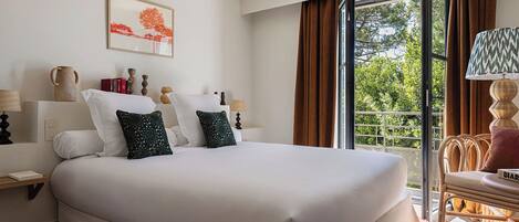 Habitación de hotel con una cama grande, una mesita de noche con lámpara, una silla y una ventana con cortinas.