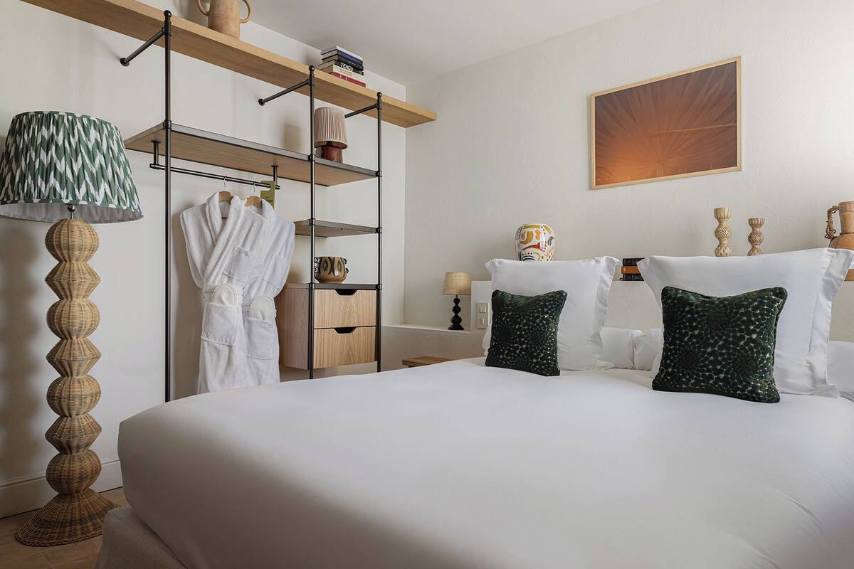 A hotel room with a large bed, a wardrobe with shelves, a lamp, and a painting on the wall.