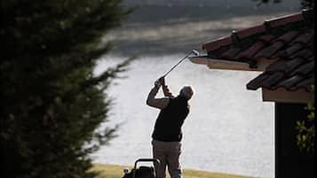 A person using a leaf blower near a house with a lake in the background.