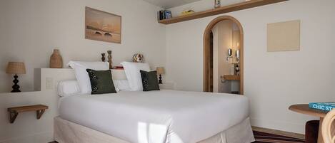 A hotel room with a large bed, a ceiling fan, a small table, and a bookshelf.
