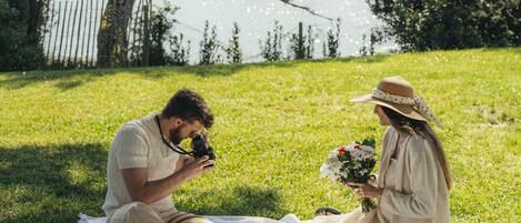 Een koppel zit op een deken aan een meer, met een camera en bloemen.