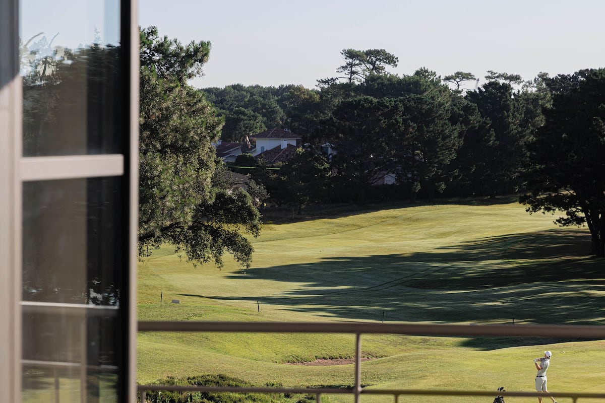 A room with a view of a golf course, a window, and a chair with a cushion.