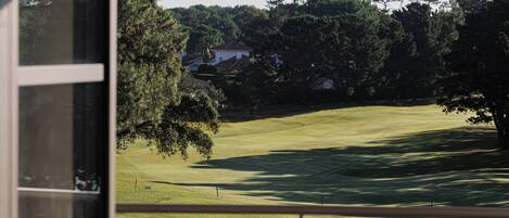 Una habitación con vistas a un campo de golf, una ventana y un sillón con cojín.