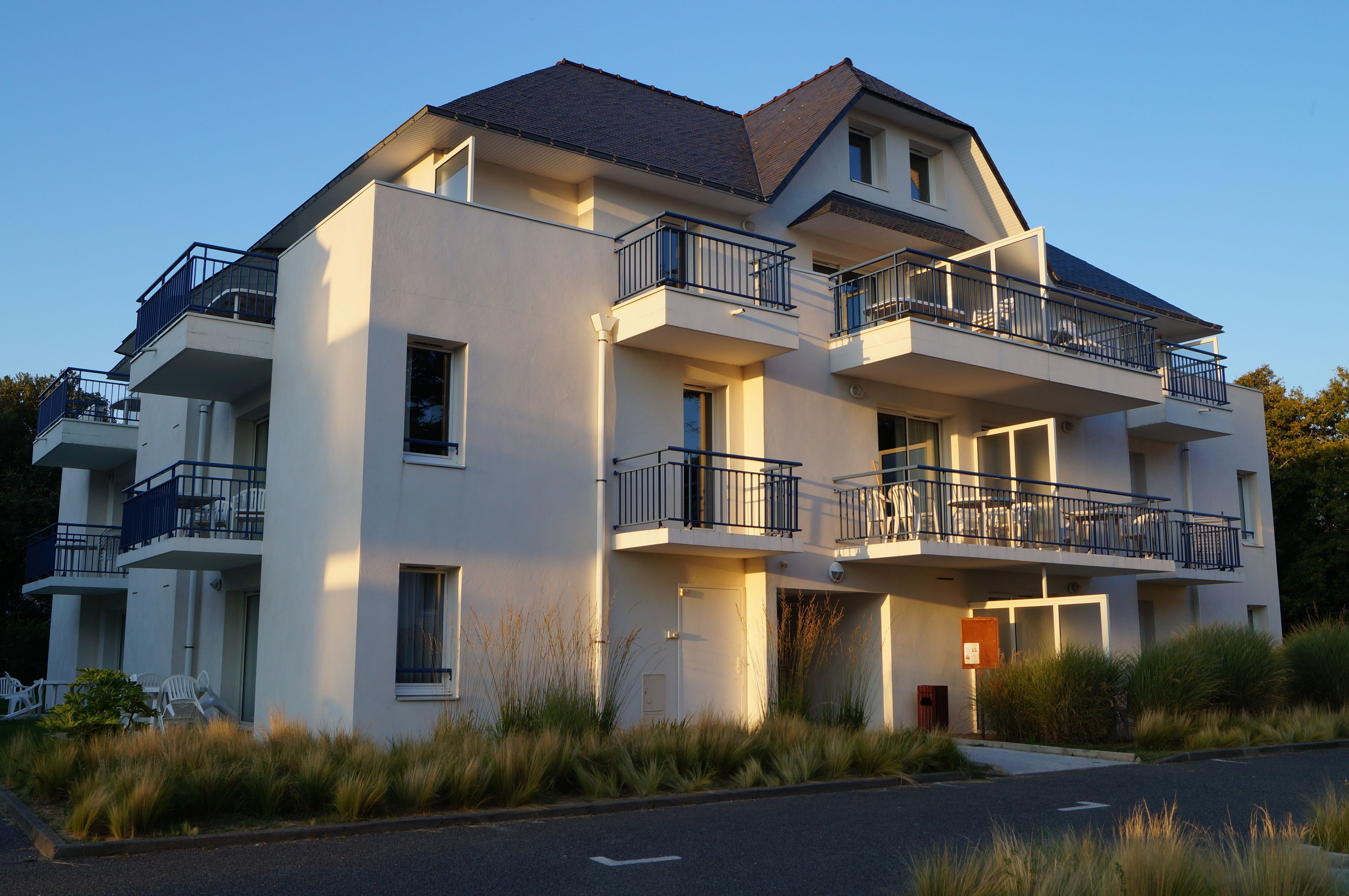 Un immeuble résidentiel à plusieurs étages, doté de balcons, d’un toit plat et d’une pelouse bien entretenue.