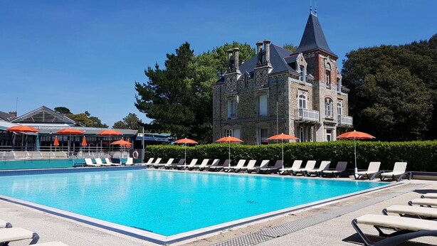 A swimming pool with lounge chairs and umbrellas, surrounded by a stone building with a tower. - Residence Ker Juliette (Pornichet)