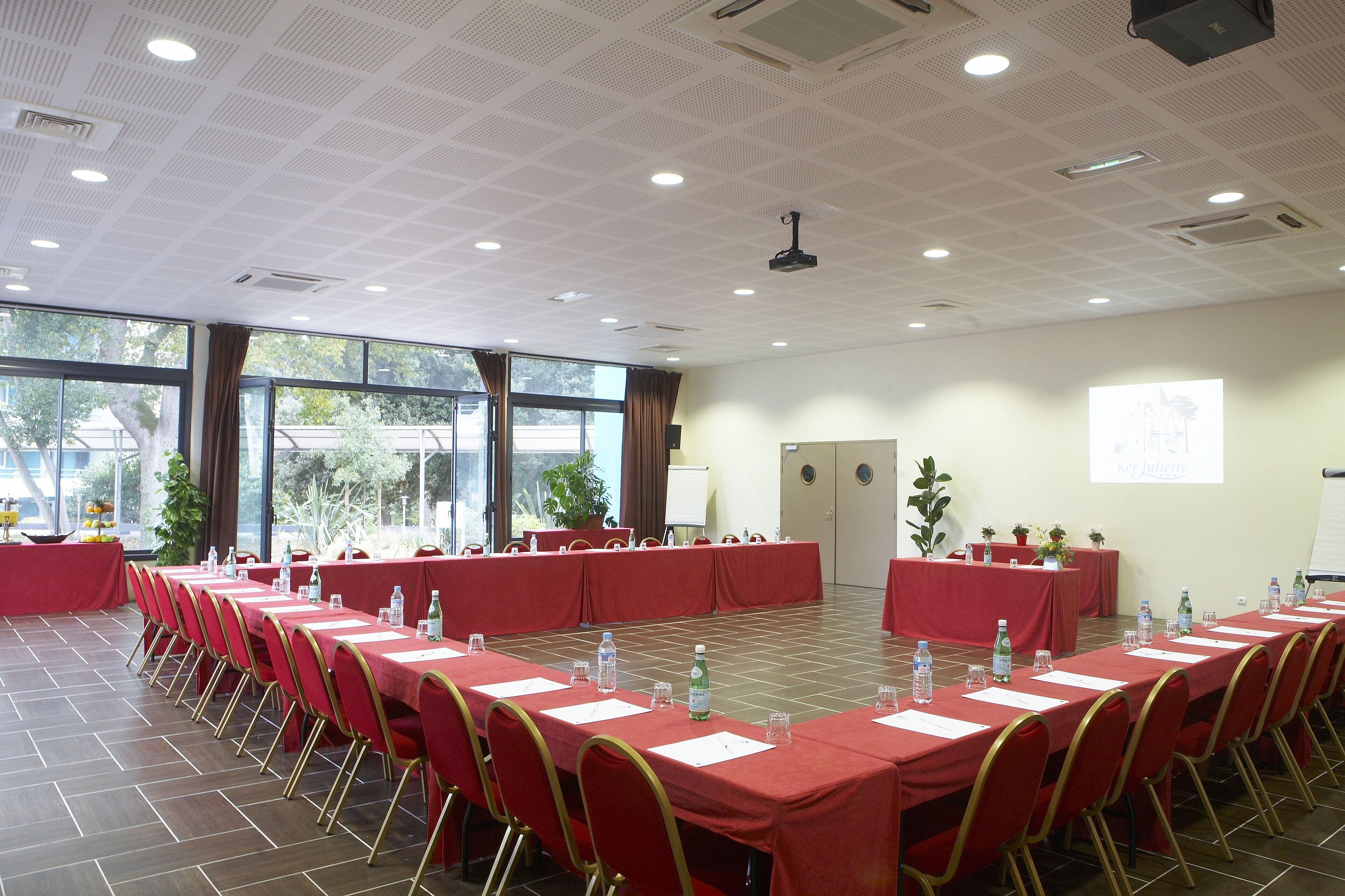 A conference room with long tables, chairs, and a projector screen.