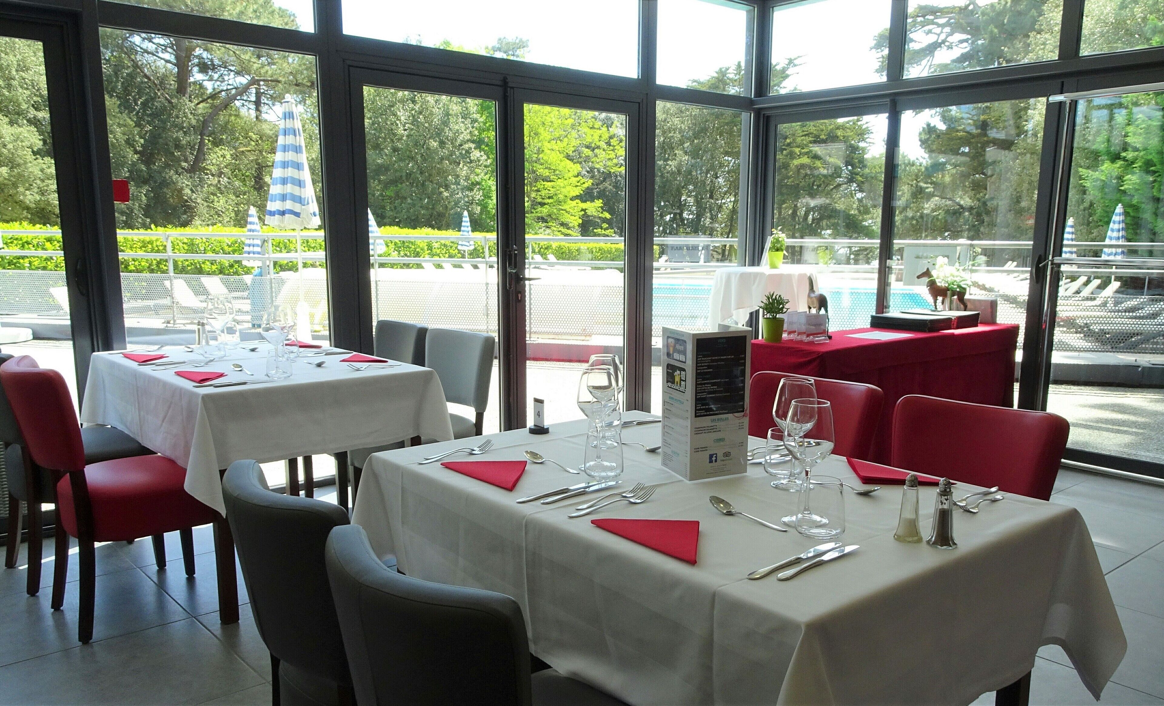 Ein Restaurant mit gedeckten Tischen, großen Fenstern und Blick auf einen Pool und Grünflächen.