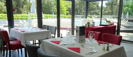 Ein Restaurant mit gedeckten Tischen, großen Fenstern und Blick auf einen Pool und Grünflächen.