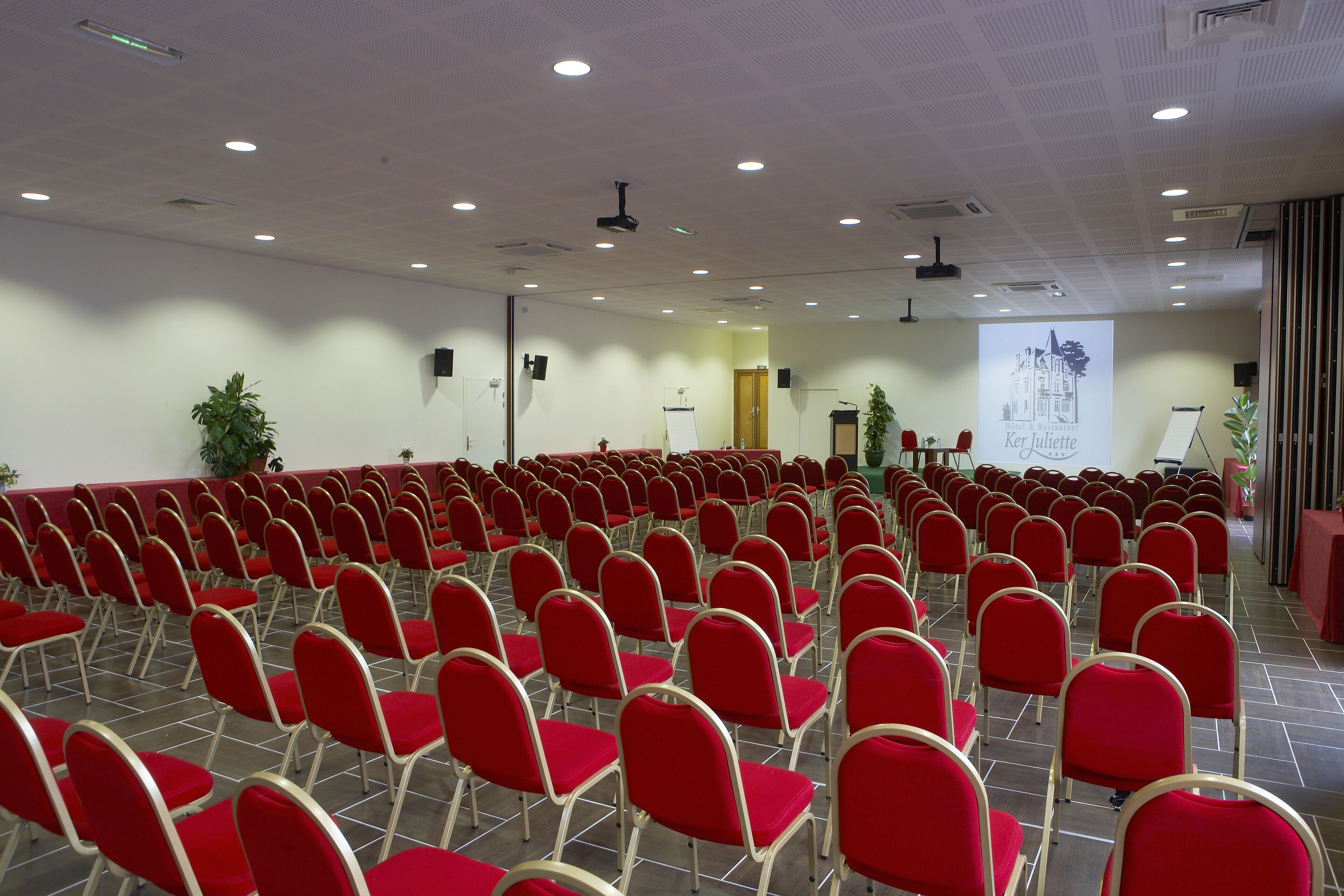 A conference room with rows of red chairs, a projector screen, and a presentation area.