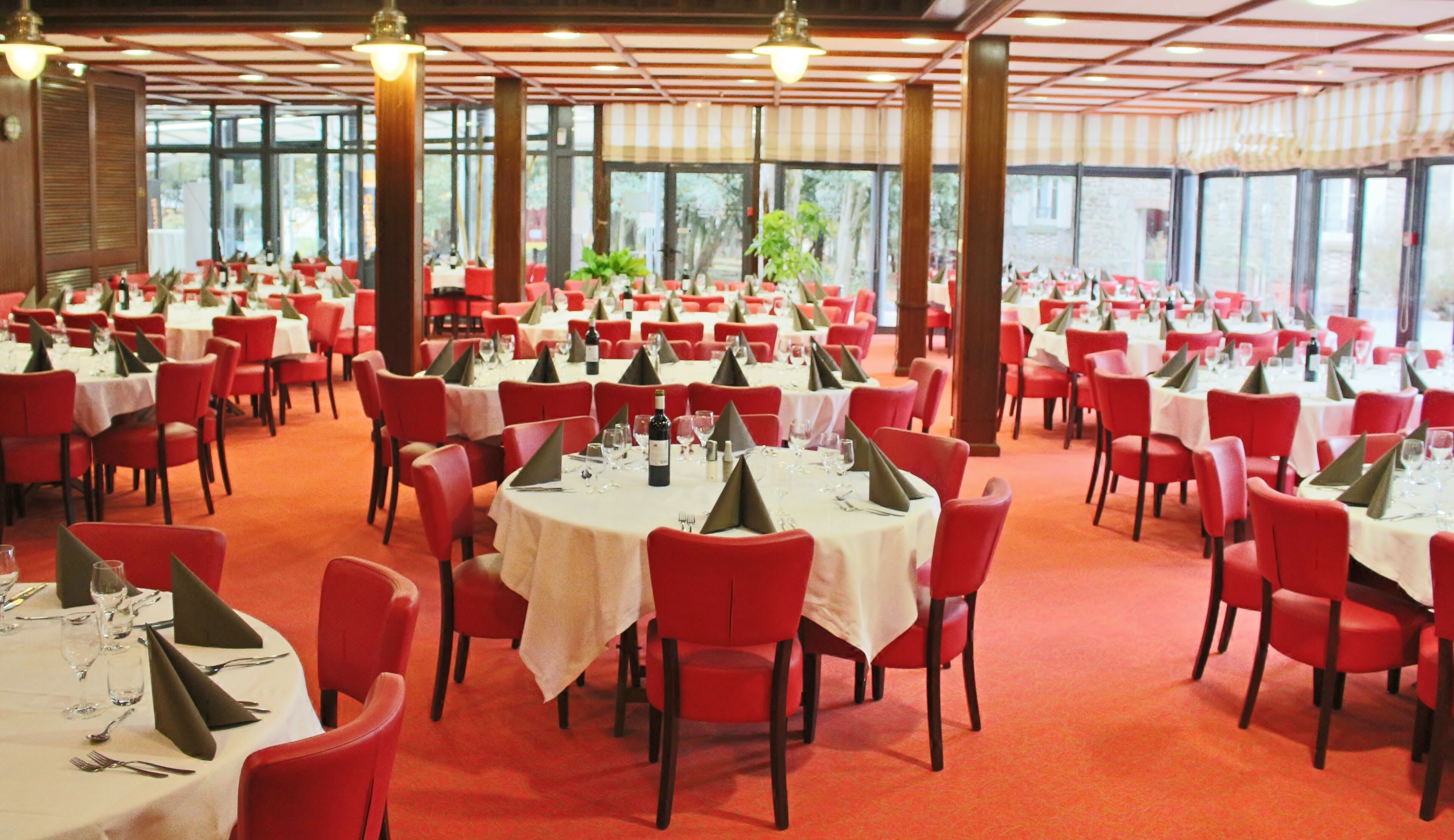 Un amplio salón de banquetes con mesas redondas cubiertas con manteles blancos, sillas rojas y centros de mesa verdes.