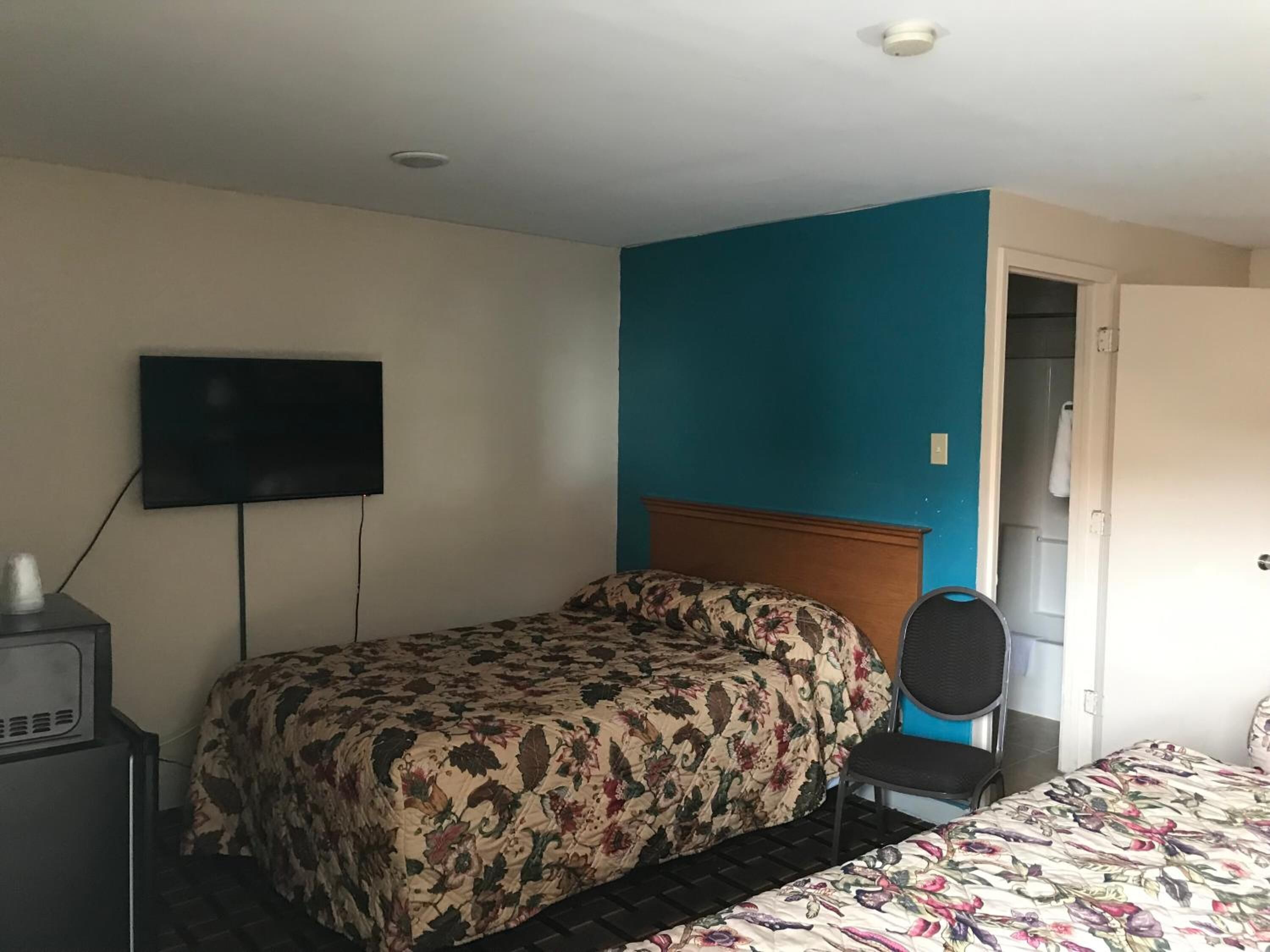 A hotel room with a bed, a TV, a chair, and a door leading to a bathroom.