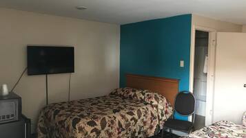 A hotel room with a bed, a TV, a chair, and a door leading to a bathroom.