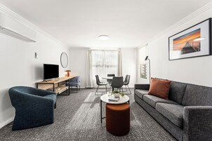A modern living room with a sofa, armchair, coffee table, TV, and dining area.