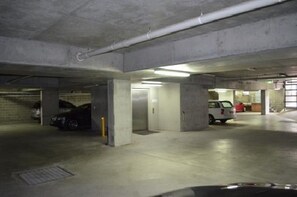 Een meerlaagse ondergrondse parkeergarage met betonnen pilaren, enkele geparkeerde auto's en een lift.